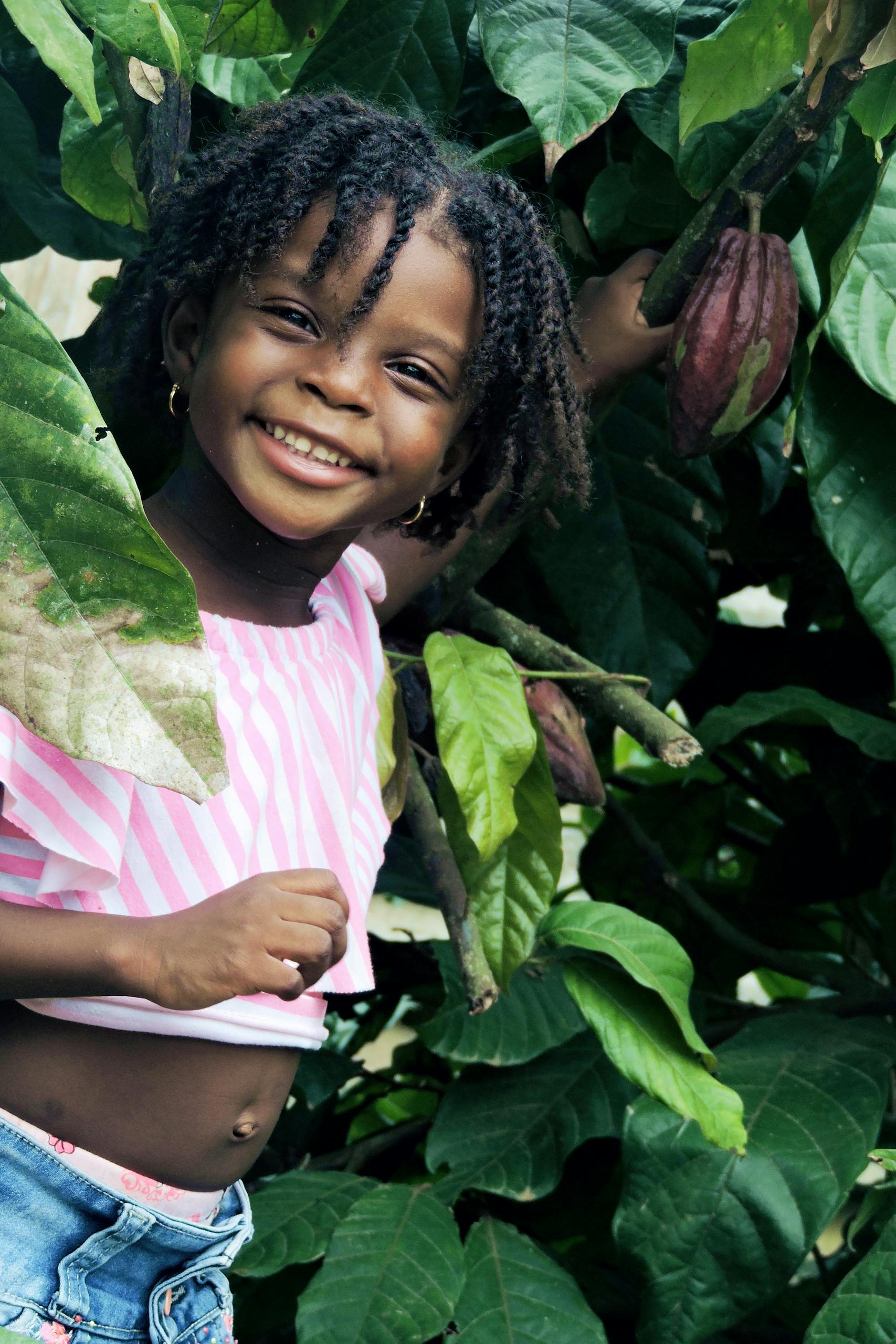 Happy African child smiling joyfully while exploring lush outdoor environment.